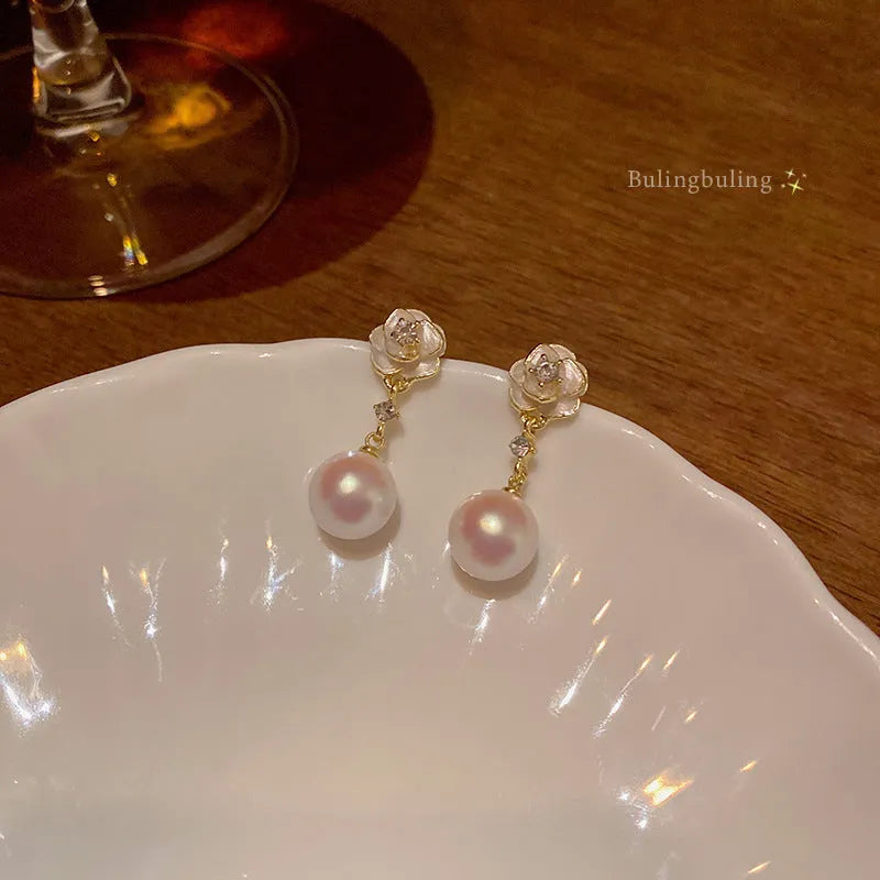 Close-up of a pair of pearl-finished camellia flower stud earrings made from alloy metal.