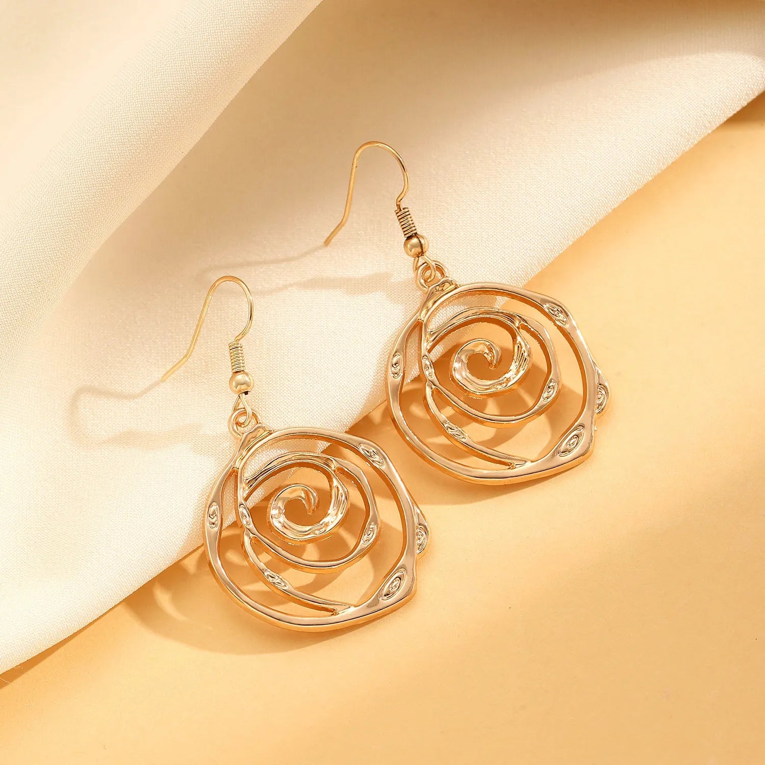 Spiral donut design necklace, bracelet, and ear hook set in gold or silver plating on a dark background.
