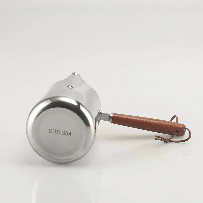 Stainless steel coffee mug with measurement scale and a light wood handle on a wooden table.
