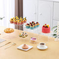 White plastic dessert table display stand with six cube-shaped racks for cakes and pastries.