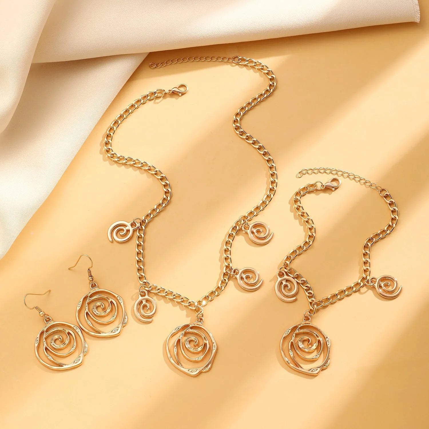 Spiral donut design necklace, bracelet, and ear hook set in gold or silver plating on a dark background.
