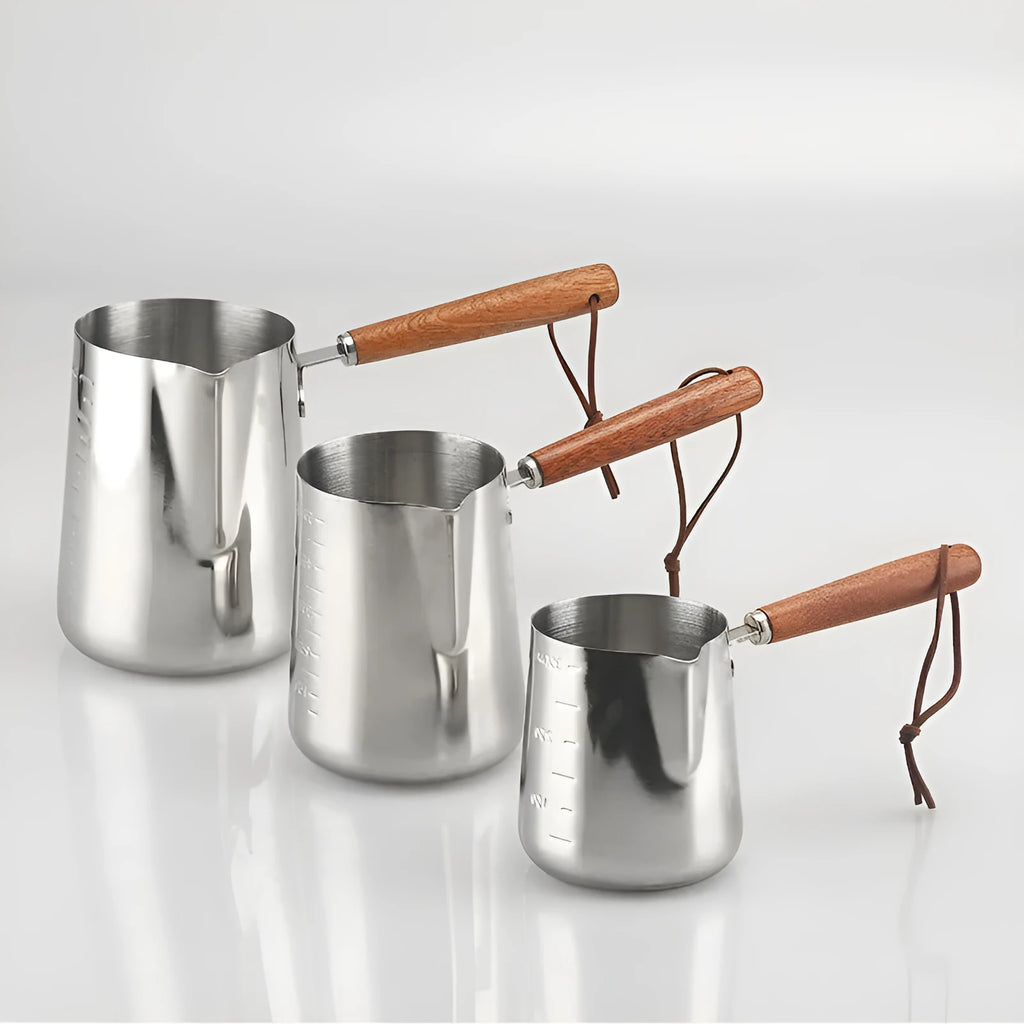 Stainless steel coffee mug with measurement scale and a light wood handle on a wooden table.