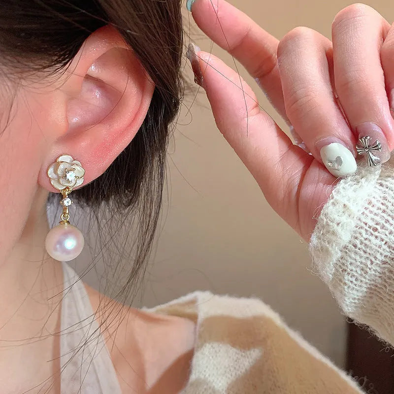 Close-up of a pair of pearl-finished camellia flower stud earrings made from alloy metal.