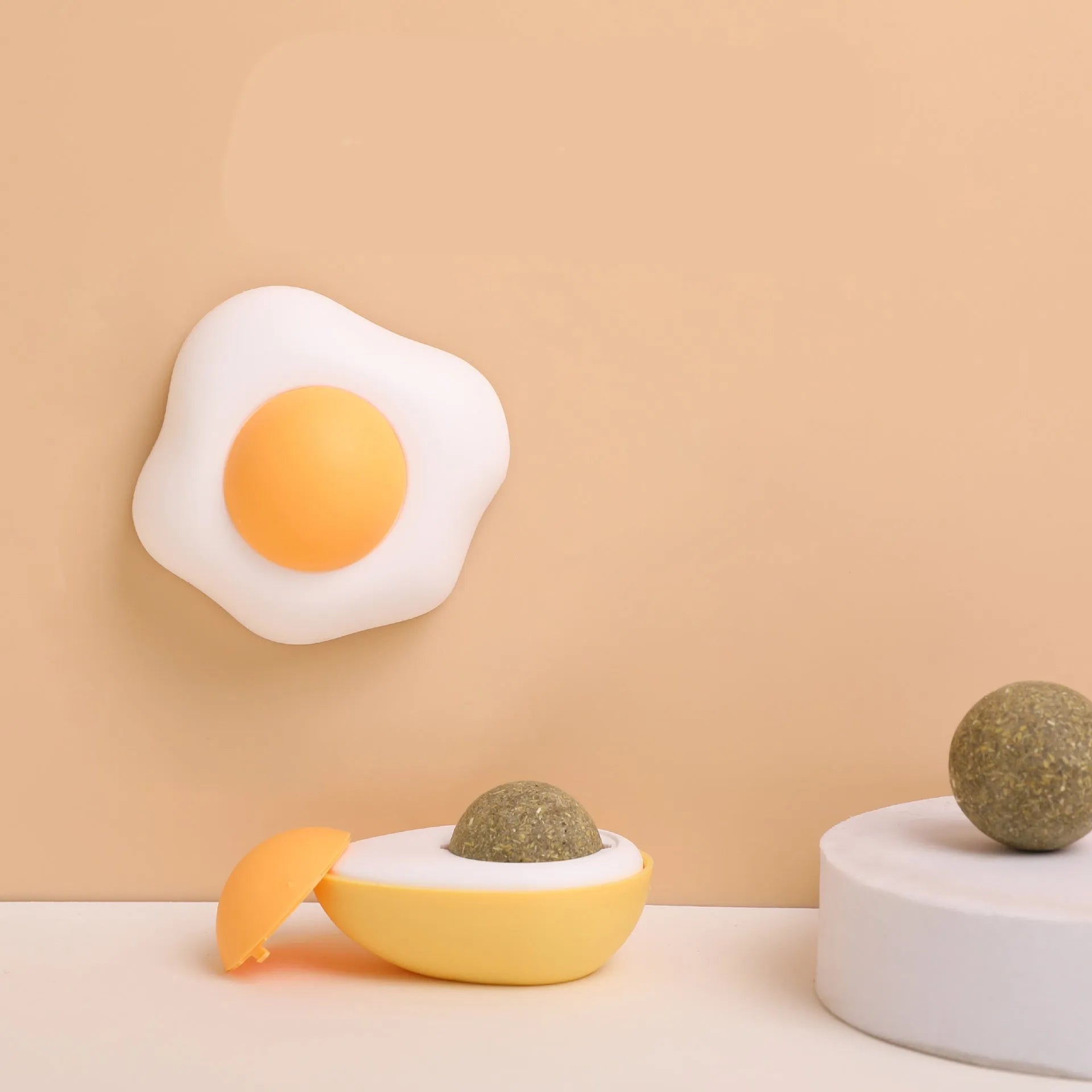 Soft plush catnip ball toy with suction cup mounted on a wall, shown in fried egg and poached egg shapes.