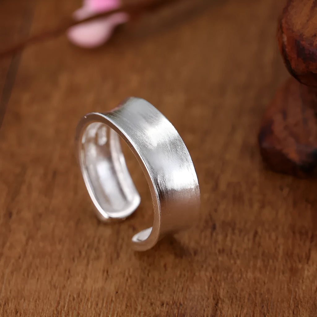 Adjustable open ring in frosted sterling silver with a geometric shape on a grey background.