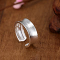 Adjustable open ring in frosted sterling silver with a geometric shape on a grey background.
