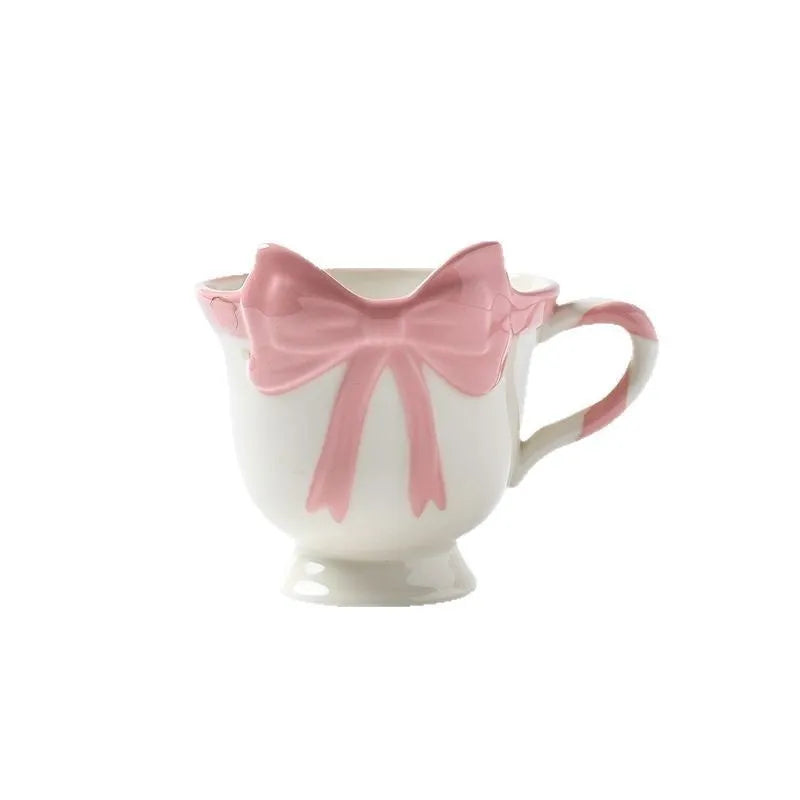Ceramic mug with a pink and white girl's heart bow decoration on the side.