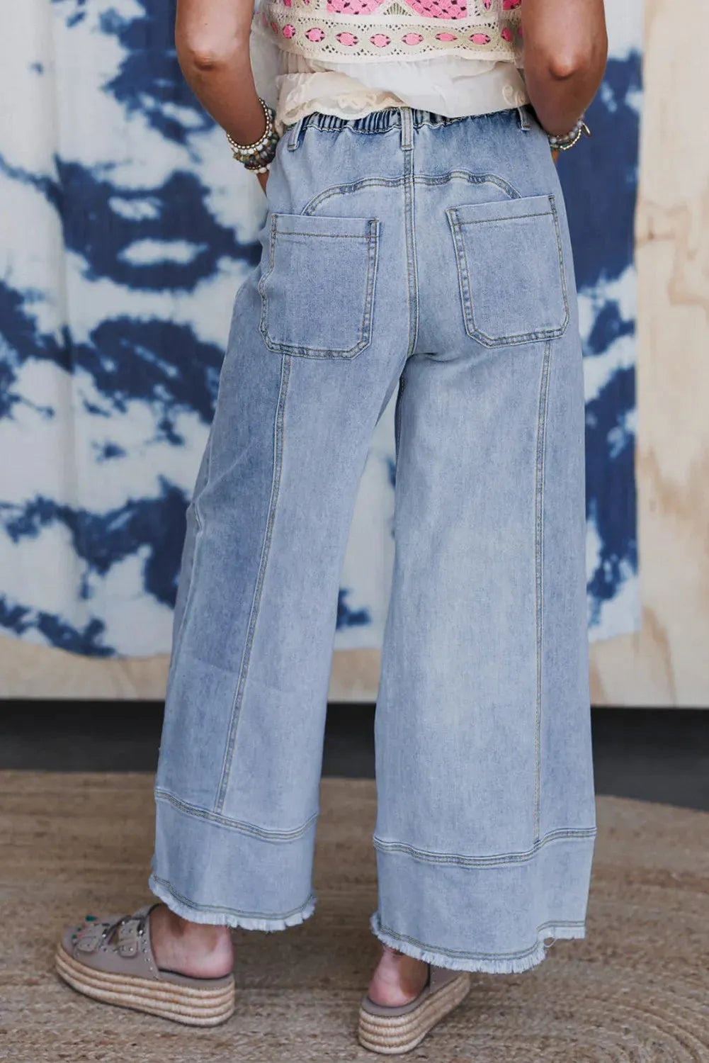 Beau blue wide leg denim trousers with drawstring waist and raw hem on a hanger