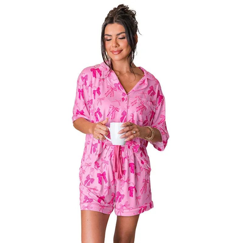 Pink women's pyjama set with bow print on V-neck top and loose trousers on a hanger