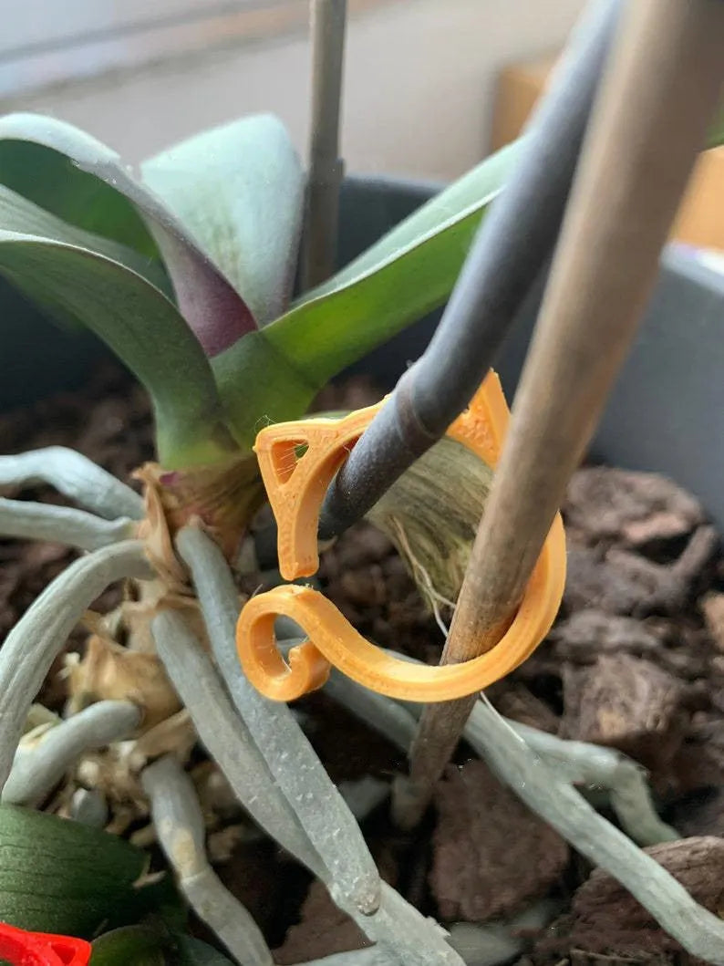 Red cat-shaped plastic gardening clip for plant support on green leaves