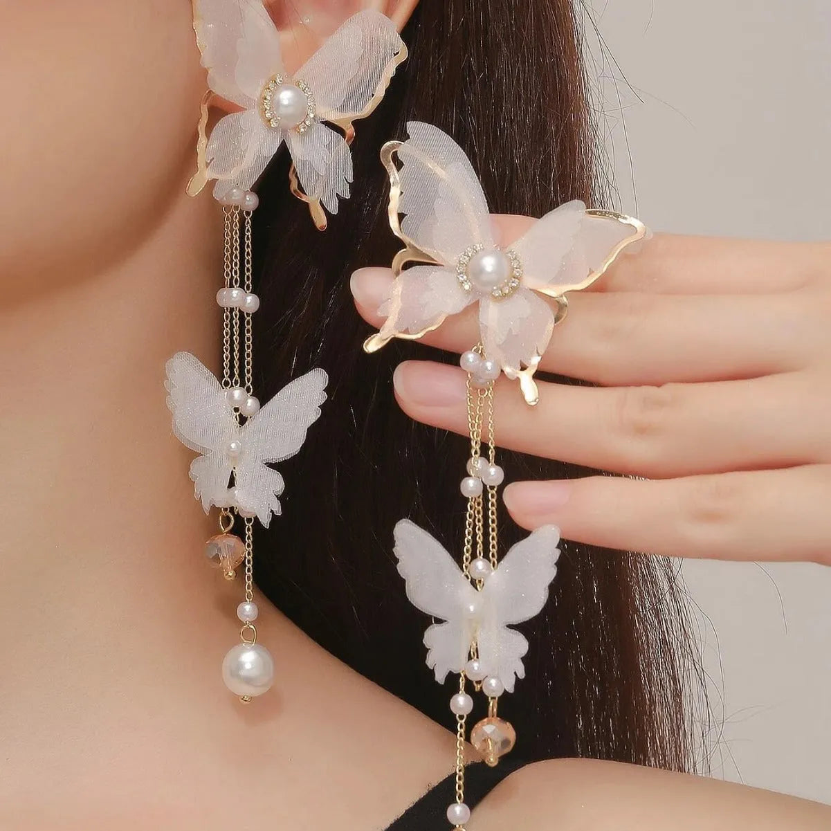 Close-up of a white butterfly-shaped earring with lace detail, pearls, rhinestones, and a long tassel.