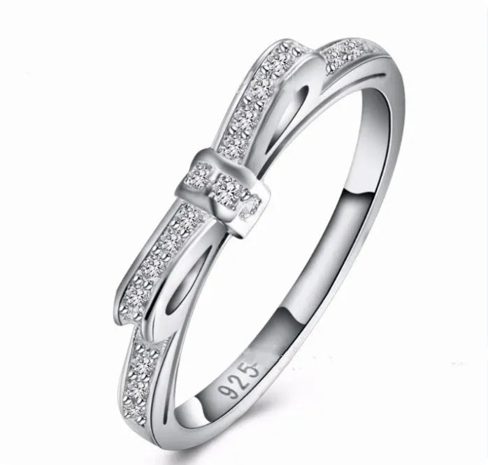 Silver-coloured bow-shaped ring with rhinestone and zircon crystal decoration on a white background.