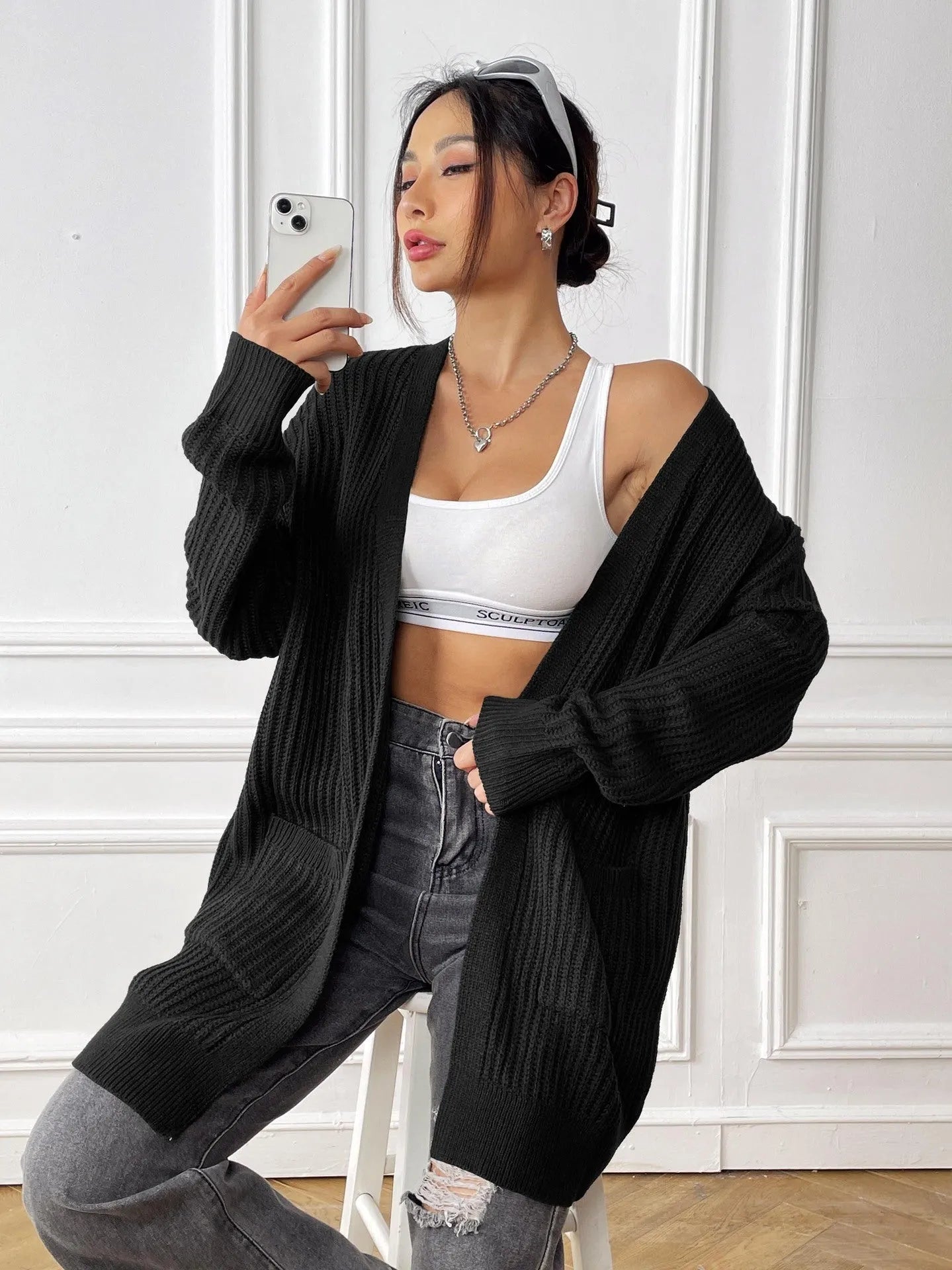 A woman wearing a loose-fitting, mid-length dark green cardigan sweater with double pockets.