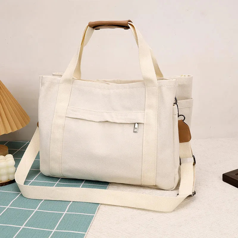 Large horizontal square canvas tote bag with cross-body strap, shown in army green colour with visible sewing lines.