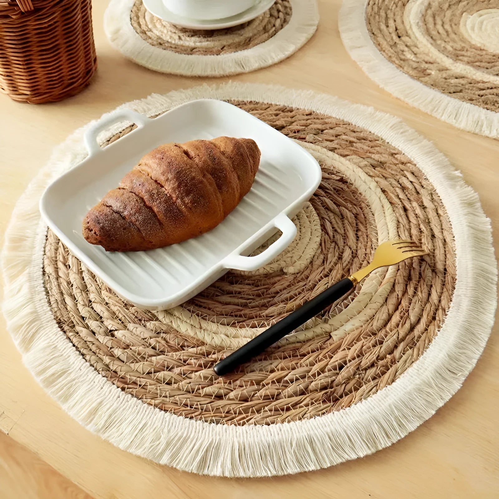 Round natural papyrus placemat with corn rope tassel trim on a wooden table.