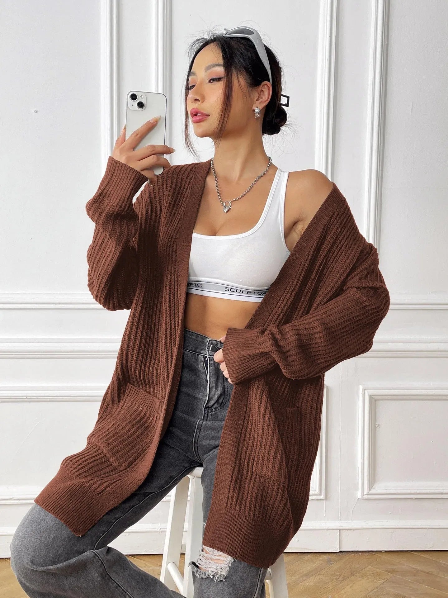 A woman wearing a loose-fitting, mid-length dark green cardigan sweater with double pockets.