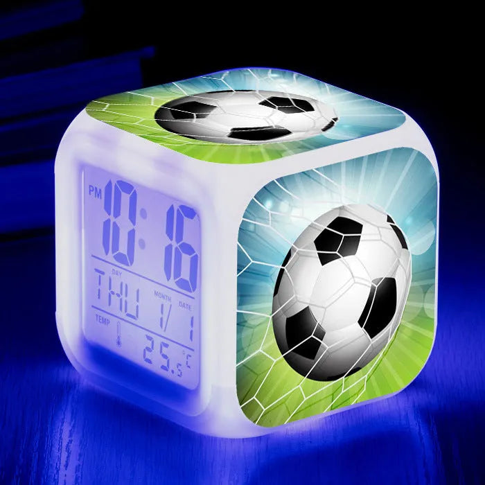 Square football-themed children's alarm clock with mute function on a desk.