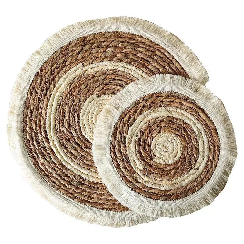 Round natural papyrus placemat with corn rope tassel trim on a wooden table.