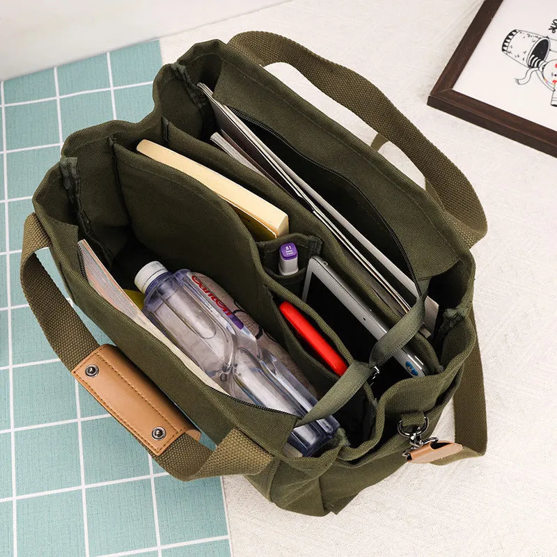 Large horizontal square canvas tote bag with cross-body strap, shown in army green colour with visible sewing lines.