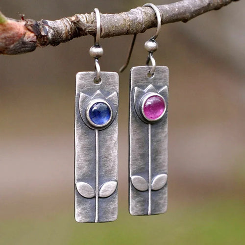 Antique finish geometric oval earrings with a red sapphire-like stone on a white background