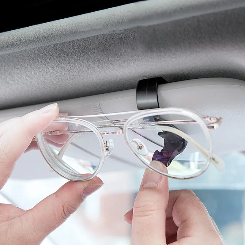 Black plastic clip for car sun visor holding a pair of glasses and a ticket.