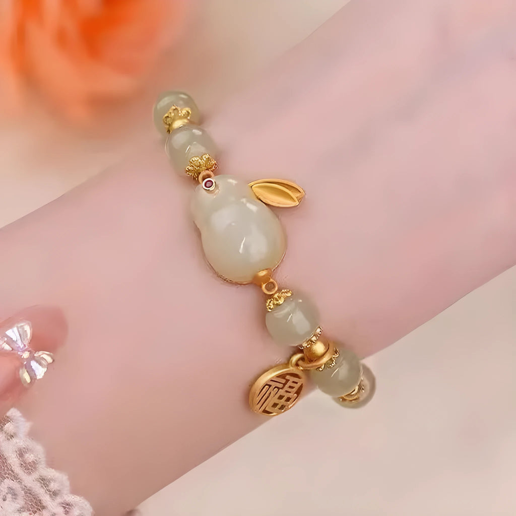 Close-up of a women's black adjustable bracelet with a green jade hare charm, fu character, and lily motif.