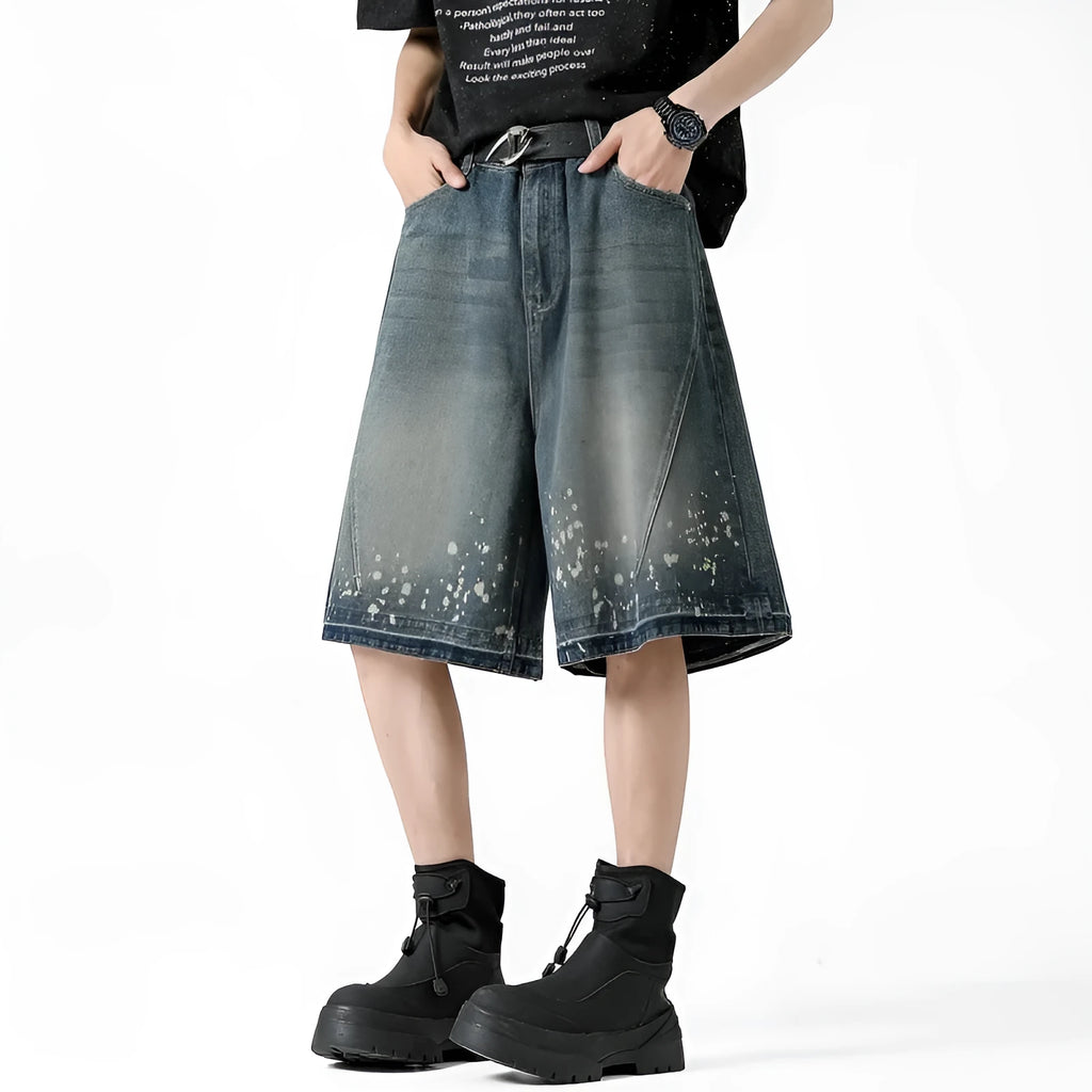 Man wearing retro blue denim shorts with ripped and splash-ink distressing on a straight-leg cut.