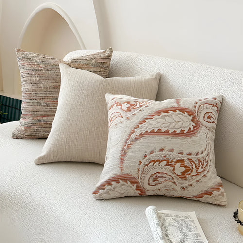 Amber coloured jacquard pillow cover with paisley and floral pattern, shown on a sofa.