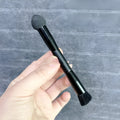 Black dual-ended concealer brush with a wooden handle and a pointed sponge applicator tip for under-eye makeup.