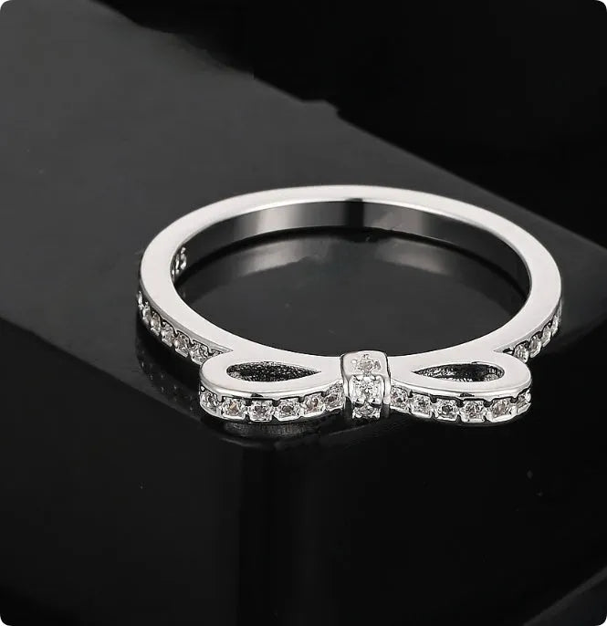 Silver-coloured bow-shaped ring with rhinestone and zircon crystal decoration on a white background.