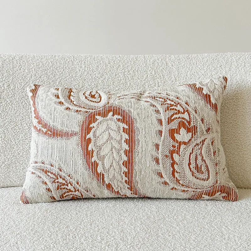 Amber coloured jacquard pillow cover with paisley and floral pattern, shown on a sofa.