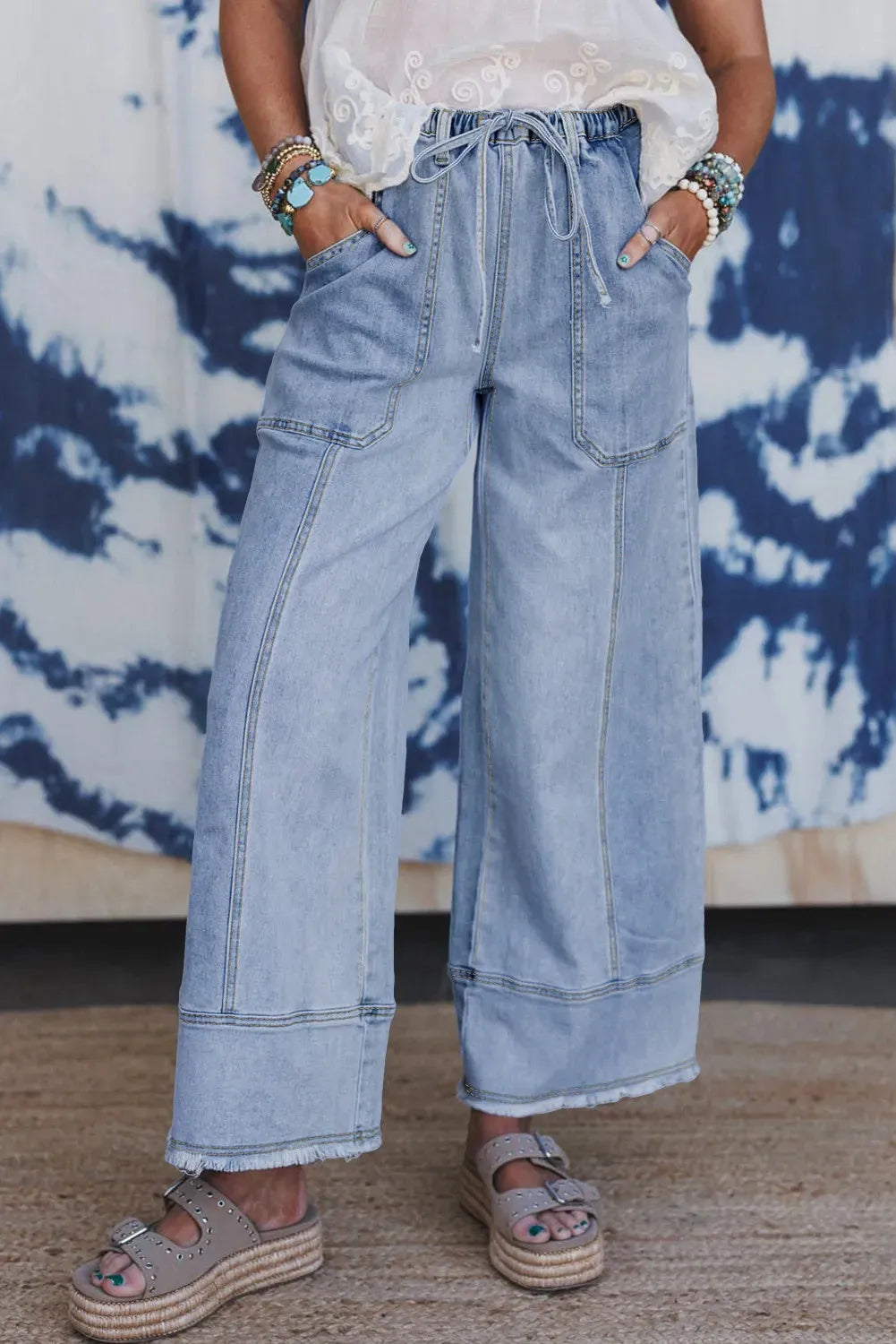 Beau blue wide leg denim trousers with drawstring waist and raw hem on a hanger