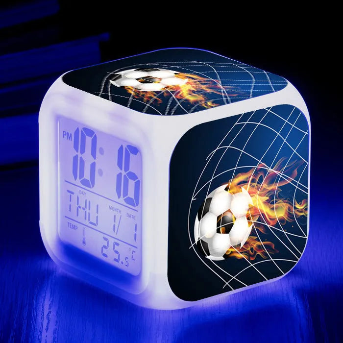 Square football-themed children's alarm clock with mute function on a desk.