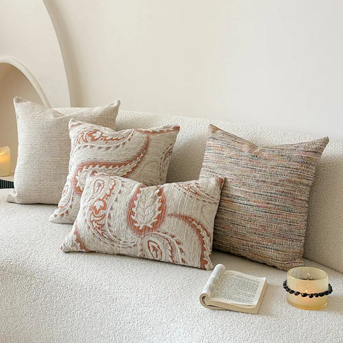 Amber coloured jacquard pillow cover with paisley and floral pattern, shown on a sofa.