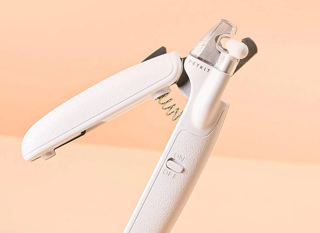 White pet nail clippers with LED light, open transparent splash guard, and separate nail file on a table