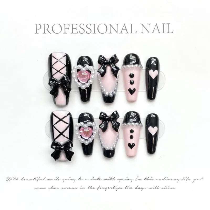 Black and pink heart-shaped press-on false nails with bow design, shown in mid-length cat's eye style.