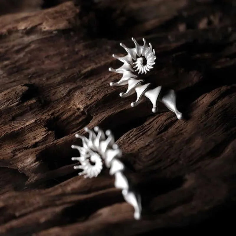 A pair of three-dimensional conch-shaped ear studs with a matte metallic finish.