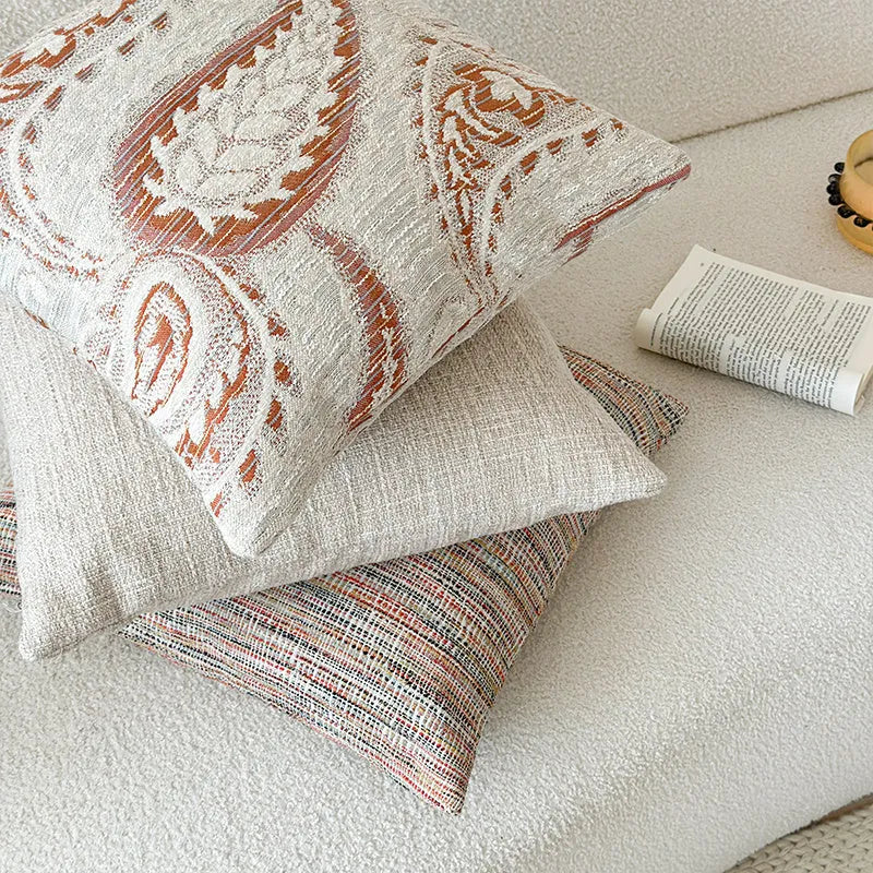 Amber coloured jacquard pillow cover with paisley and floral pattern, shown on a sofa.
