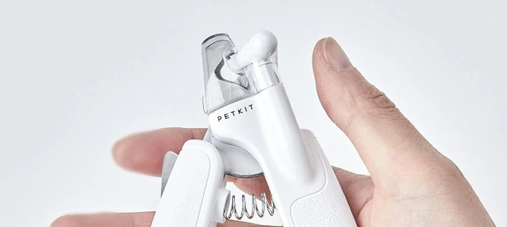 White pet nail clippers with LED light, open transparent splash guard, and separate nail file on a table