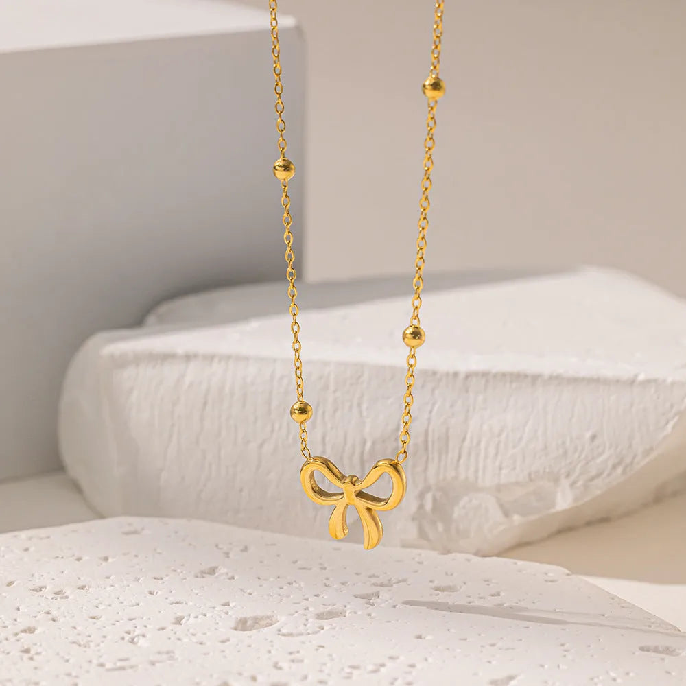 Gold electroplated bow necklace with adjustable chain on white background