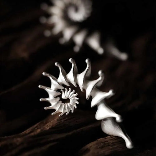 A pair of three-dimensional conch-shaped ear studs with a matte metallic finish.