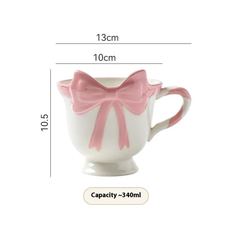 Ceramic mug with a pink and white girl's heart bow decoration on the side.