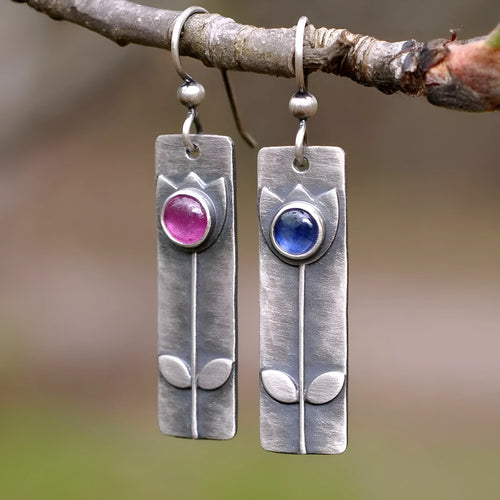 Antique finish geometric oval earrings with a red sapphire-like stone on a white background