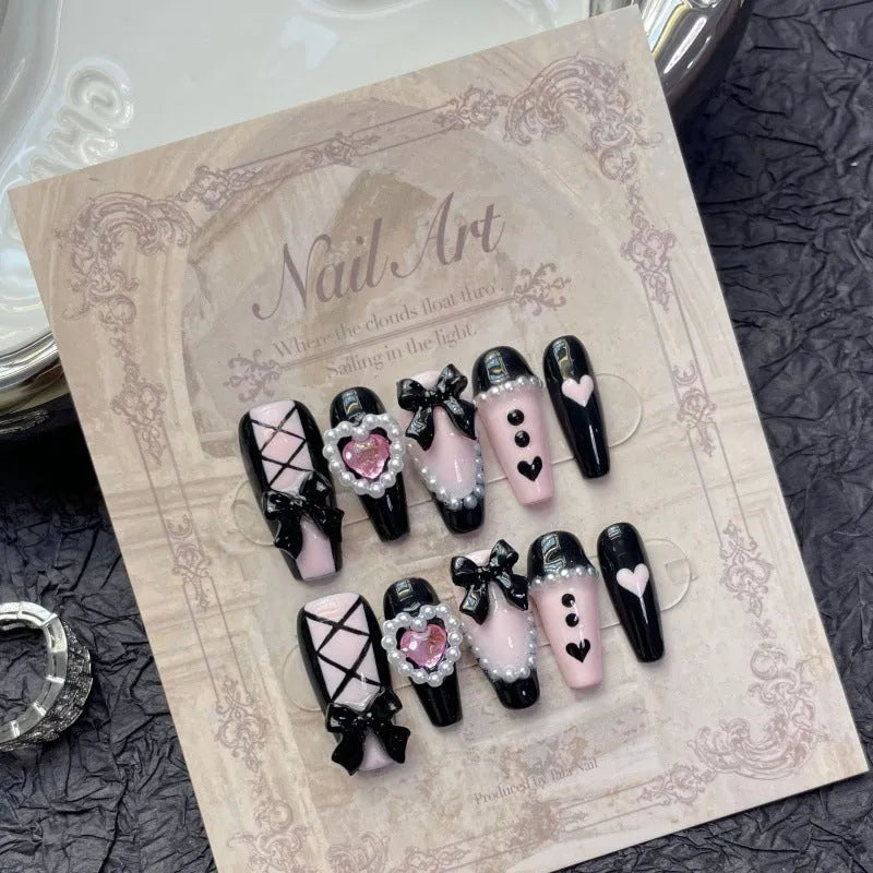 Black and pink heart-shaped press-on false nails with bow design, shown in mid-length cat's eye style.